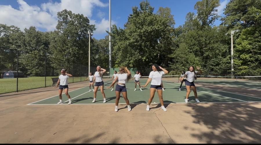 The team smiling and dancing through a routine outdoors
